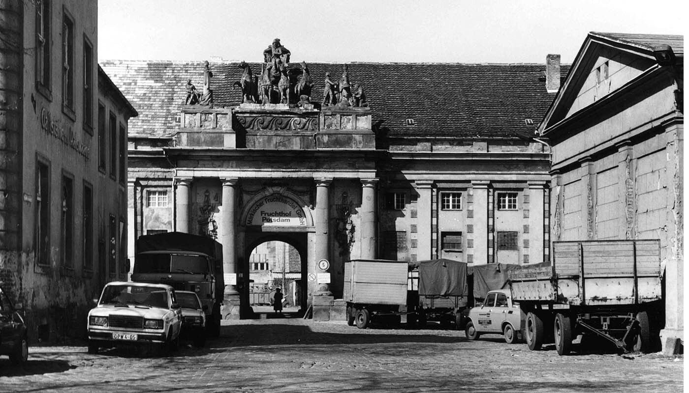Historisches Foto: Der restaurierungsdürftige Kutschpferdestall und davor Autos und kleine Lastwagen der 90er Jahre.
