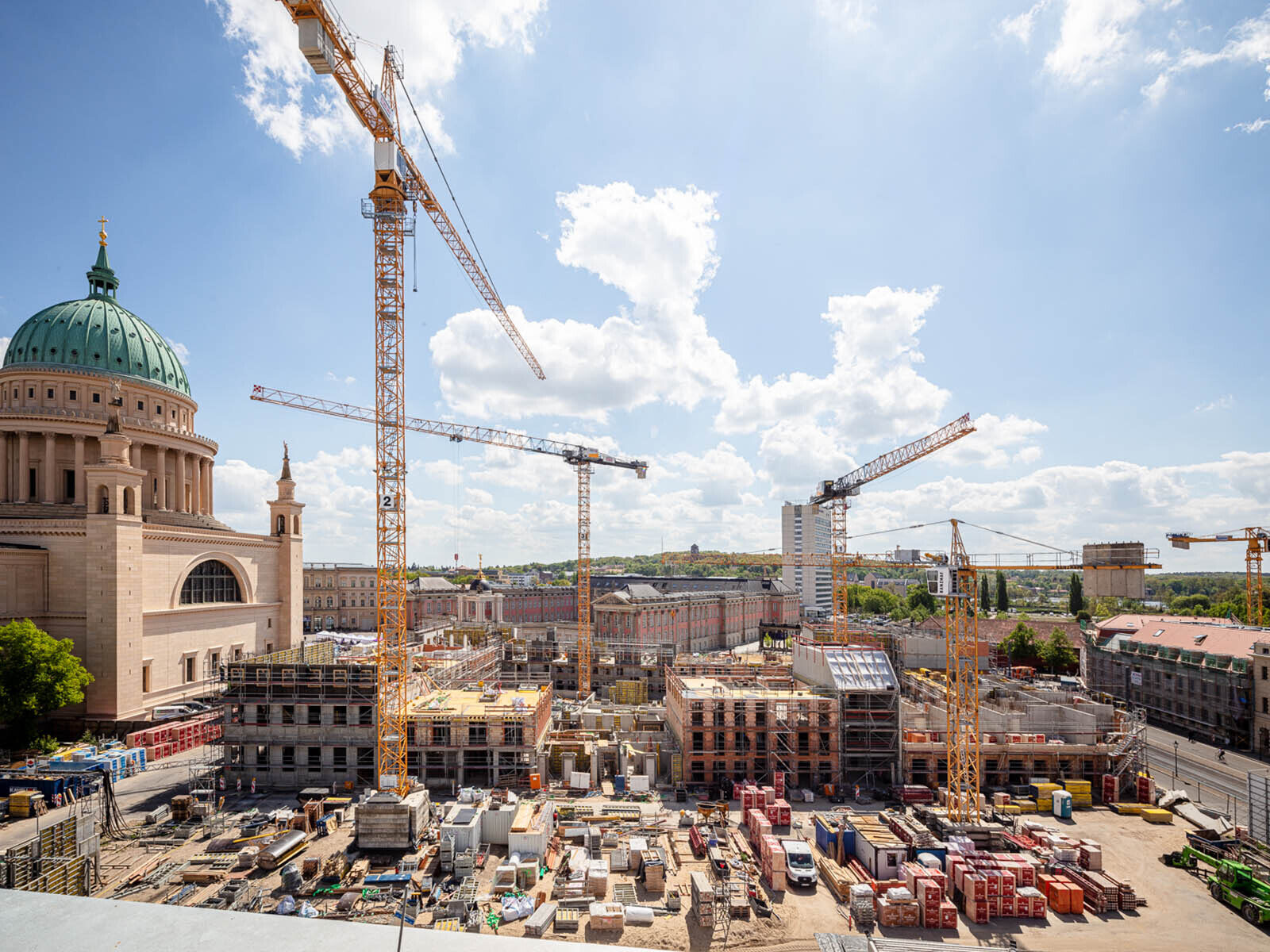 Foto: Blick vom Bildungsforum auf die Baustelle Block III. Zu sehen sind Baumaterialien, Kräne und begonnene Hochbauarbeiten, links davon die Nikolaikirche und im Hintergrund der Landtag.