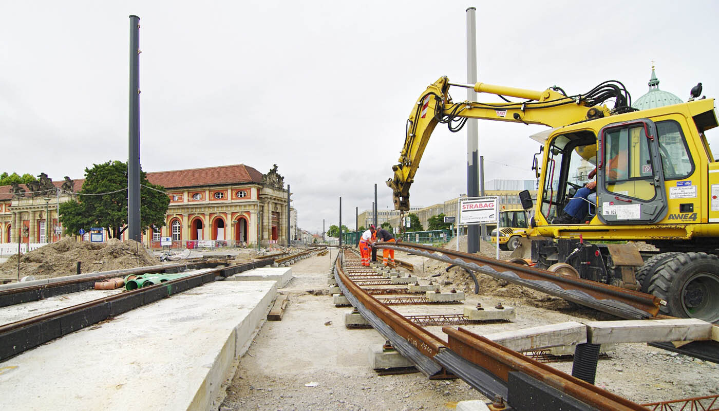 Foto: Gleisbau neben dem Filmmuseum, Bauarbeiter platzieren mit Hilfe eines Baufahrzeugs die Gleiselemente.
