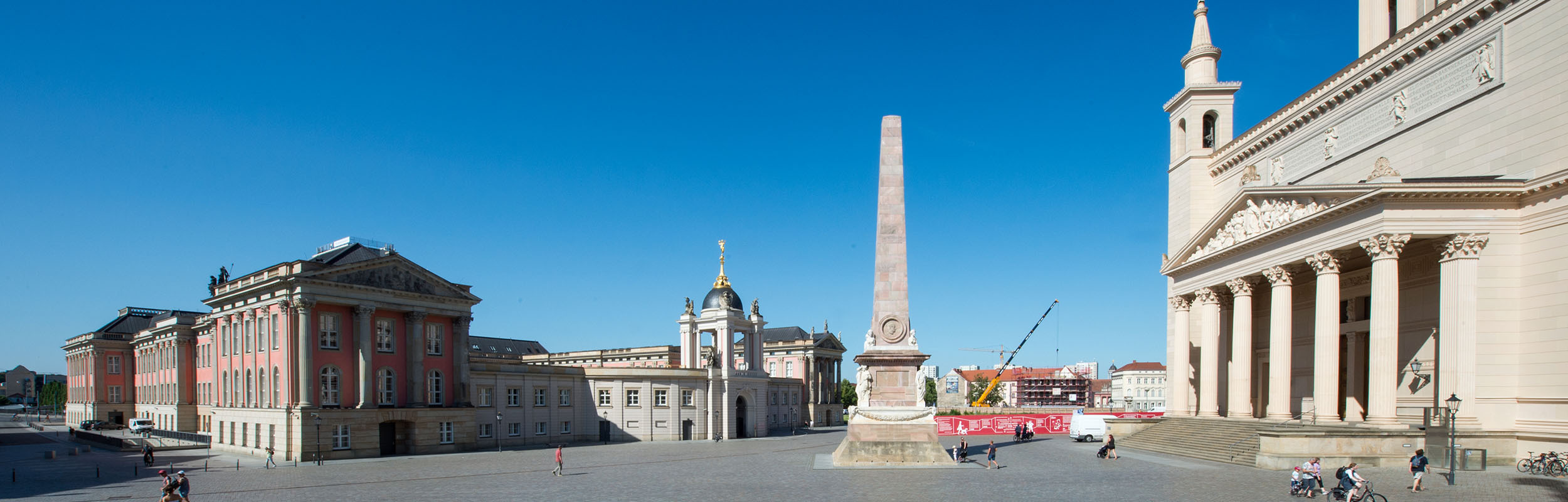 Foto: Unter blauem Himmel finden sich links der Landtag mit Fortunaportal, mittig der Obelisk, rechts der Portikus der Nikolaikirche und im Hintergrund Bauzaun und Kran von Block III.