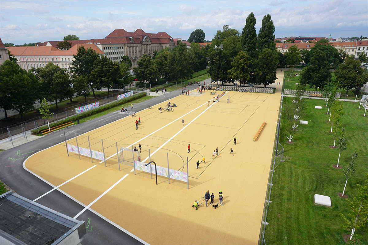 Foto: Die gelbe Sportplatzfläche und großzügige Grünfläche umschlossen von der Asphaltlaufbahn